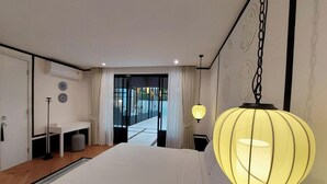 A hotel room with a bed, bedside table, lamp, and a view through a glass door to the outside. - Wild seaview pool 2bedroom villa 118 (Phuket)