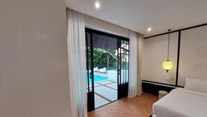 A modern bedroom with a large bed, a view of a swimming pool, and a sliding glass door leading to an outdoor area. - Wild seaview pool 2bedroom villa 118 (Phuket)