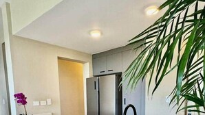 Una cocina moderna con una isla central, dos taburetes de madera, un refrigerador de acero inoxidable y un lavamanos.