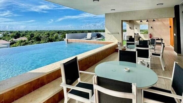 Un área de comedor exterior moderna con vista a la piscina, con una mesa redonda y sillas blancas.