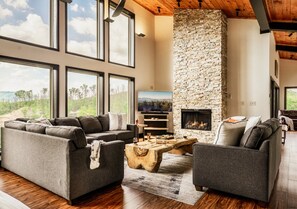 A spacious living room with a stone fireplace, large windows, and a view of the outdoors. - Private Pool Cabin w/ Theater, Hot Tub & Views (Sevierville)