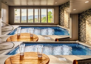 A spa area with a pool, wooden seating, and large windows offering a view of the outdoors. - Private Pool Cabin w/ Theater, Hot Tub & Views (Sevierville)