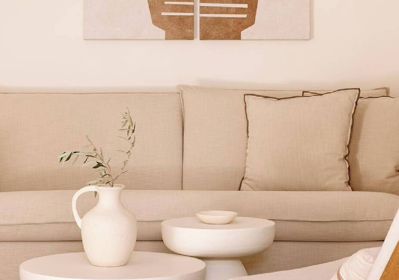 Een minimalistische woonkamer met een beige bank, een witte salontafel en een witte vaas met een plant.