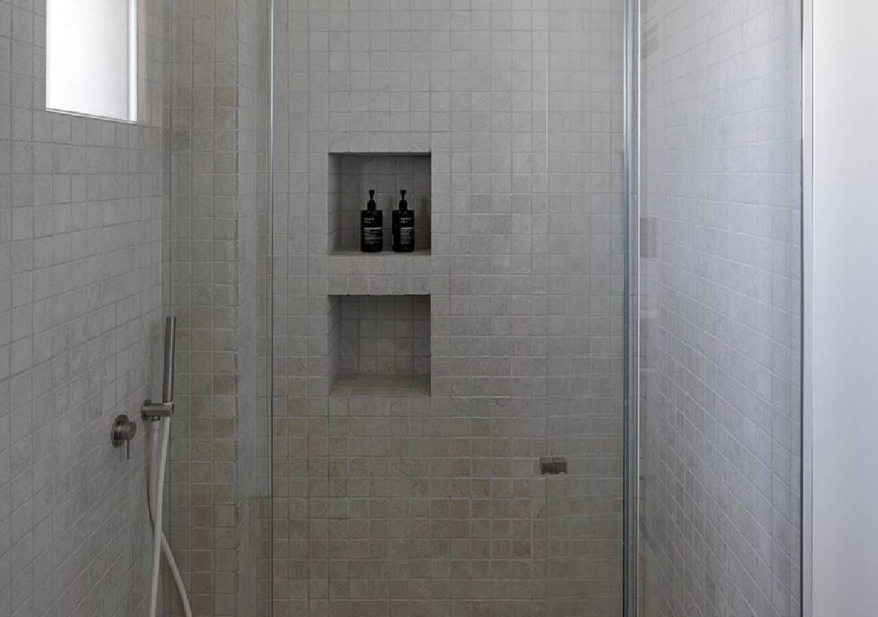 Zona de ducha con paredes de azulejos, puerta de vidrio y dos botellas en un estante.