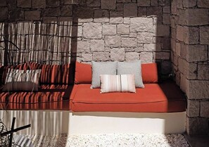 A stone wall with a built-in bench and cushions. - The Village by WPS (Milos)