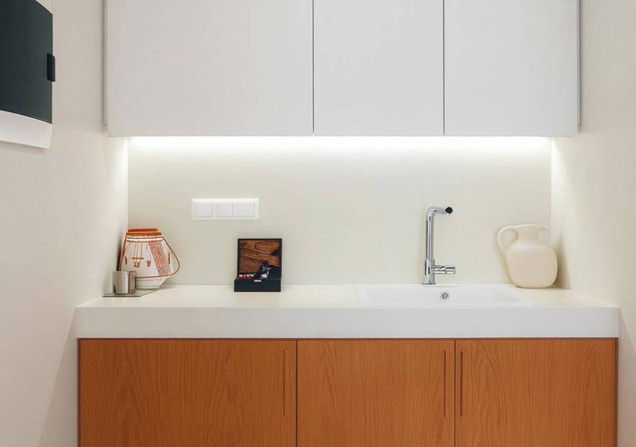 Un baño moderno con un lavamanos blanco, armarios de madera y un espejo encima.