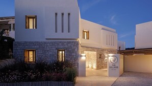 A modern villa with a stone facade, a welcoming entrance, and a sign reading "The Village Milos." - The Village by WPS (Milos)