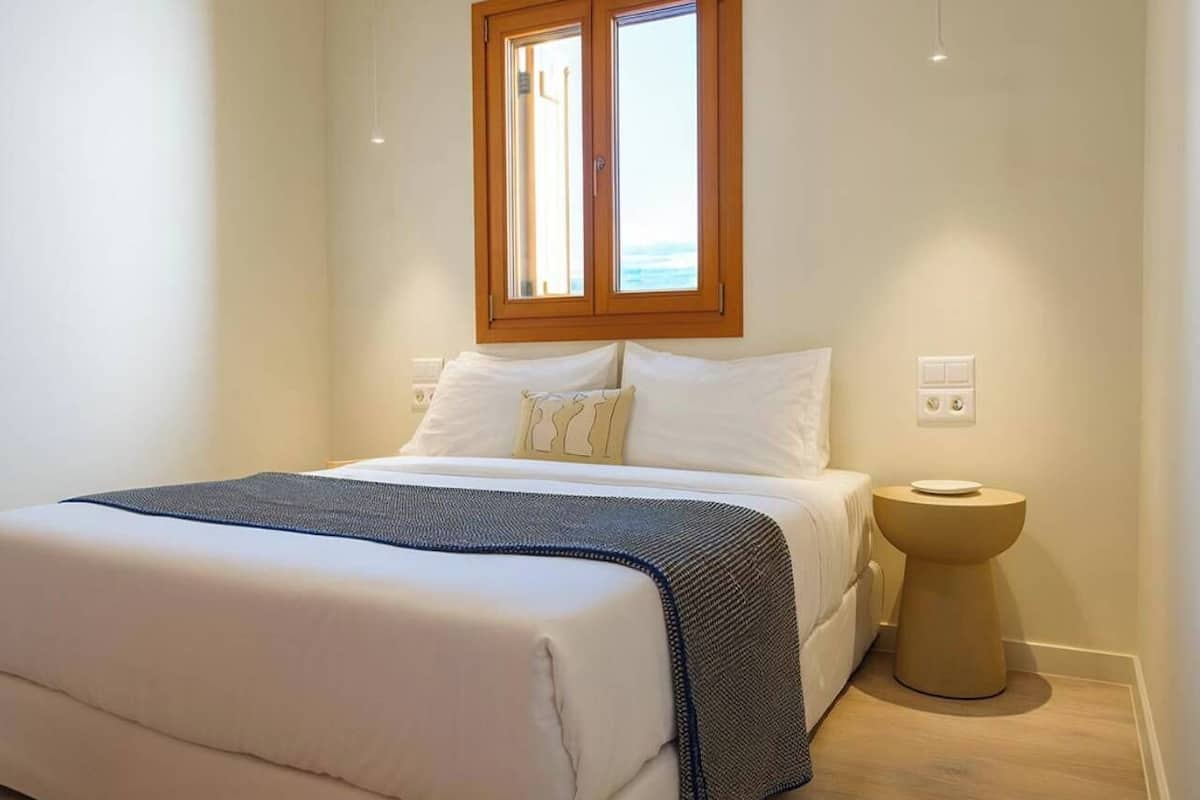 Un dormitorio con cama, mesita de noche, ventana y enchufe.