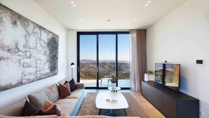 A modern living room with a large window, a sofa, a coffee table, and a TV. - Lovely 2BR Villa with Pool in Cyprus (Tsada)