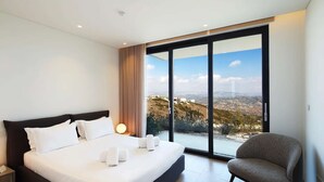 A modern hotel room with a large bed, a view of the city, and a chair. - Lovely 2BR Villa with Pool in Cyprus (Tsada)