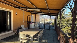 En udendørs terrasse med et bord, stole, gelænder og udsigt til bjergene.