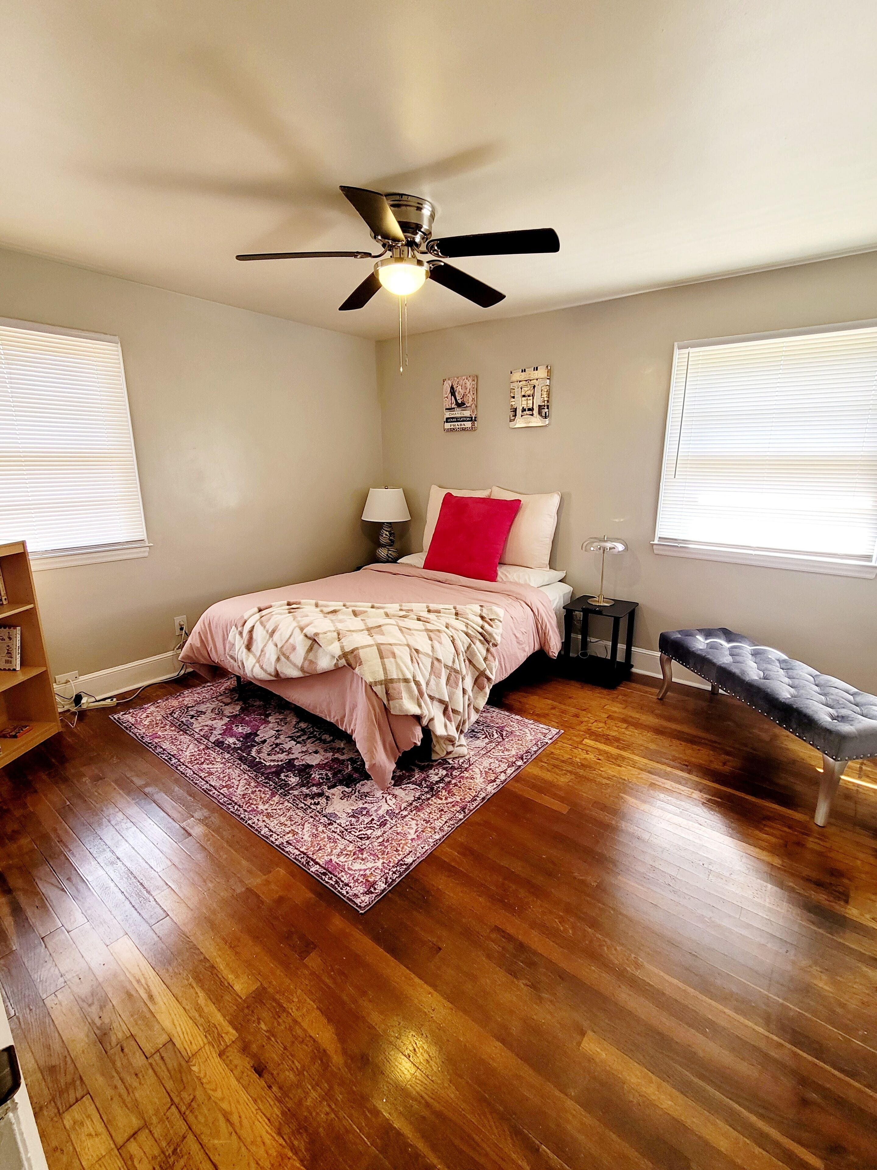 A bedroom with a bed, a ceiling fan, a nightstand, a bench, and a rug.