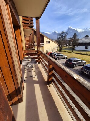 A wooden balcony with a view of snow-capped mountains, a carport with parked cars, and a building with a sloped roof. - Cozy Little Nest in Morillon, Just 50m from the Cable Cars (Morillon)
