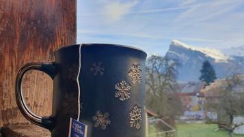 Une tasse noire ornée de motifs en forme de flocons de neige, posée sur une étagère en bois.