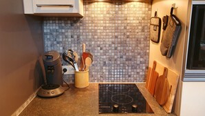 Una cocina con salpicadero de azulejos, cafetera, especiero y tablas de cortar de madera.