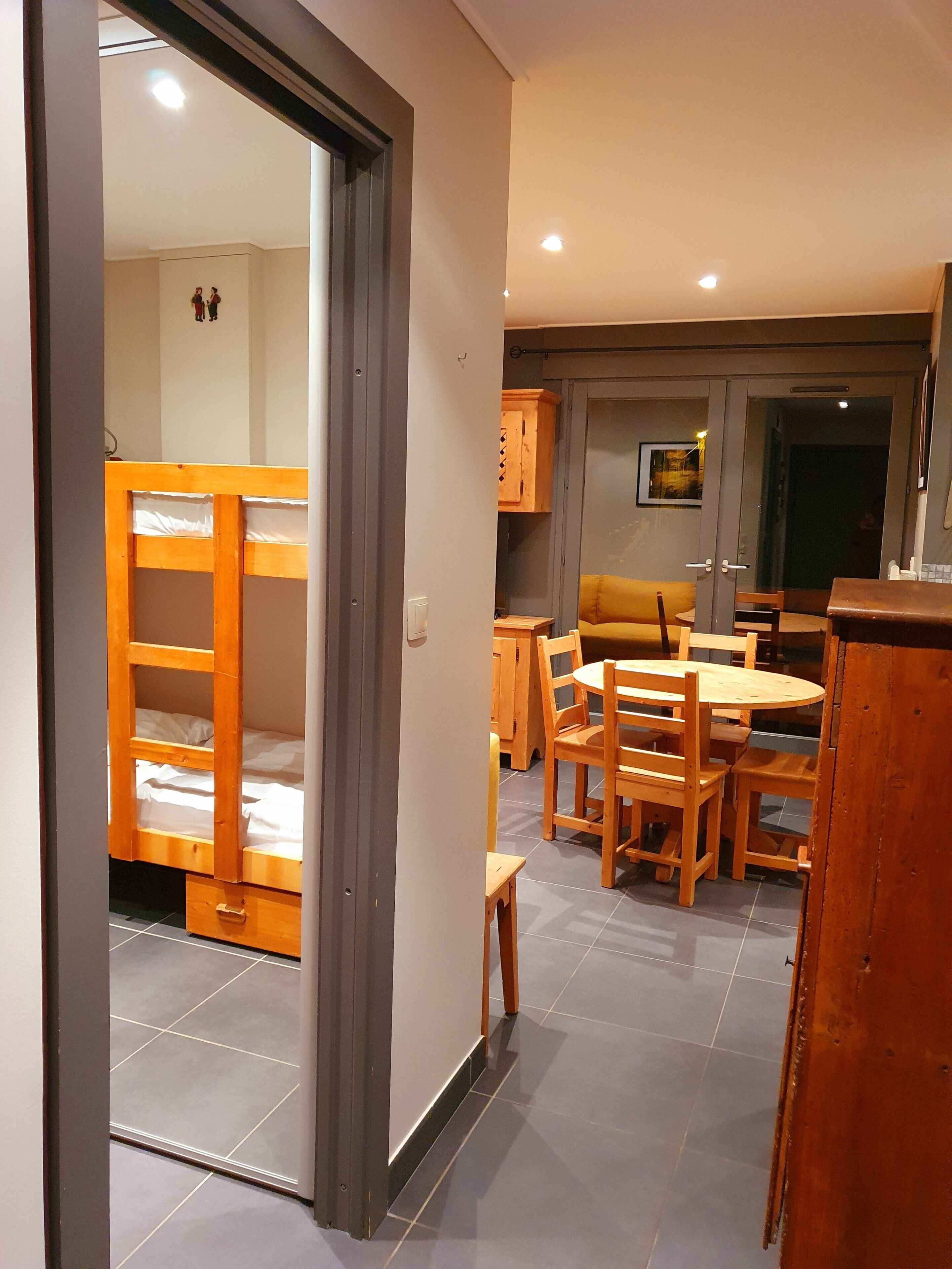 Una habitación con literas, una mesa de comedor de madera, sillas y armarios.