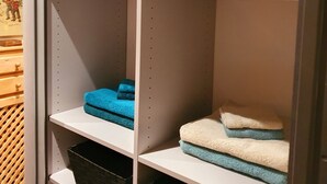 Un armario con estanterías blancas, algunas con toallas dobladas, y una zona de listones de madera.