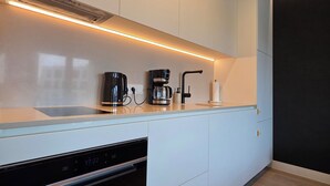 A modern kitchen with white cabinetry, a built-in oven, a coffee maker, and a sleek countertop. - Riverside Luxury Studio AC, Balcony, Fast WIFI, Steps to Market Square (Wrocław)