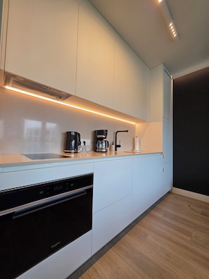 A modern kitchen with white cabinetry, a built-in oven, a coffee maker, and a sleek countertop.