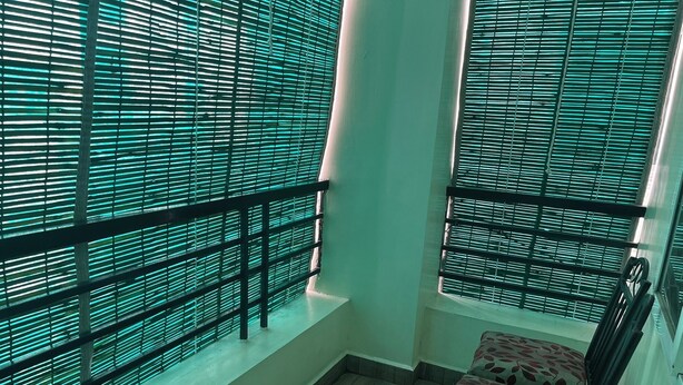 A room with a wooden floor, a chair with a leaf pattern, and a window with horizontal blinds. - Premium 2BHK• Clean & Central • Walk to IT Hub (Hyderabad)