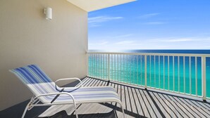 Ein Balkon mit zwei gestreiften Liegestühlen, einem weißen Geländer und Blick aufs Meer.