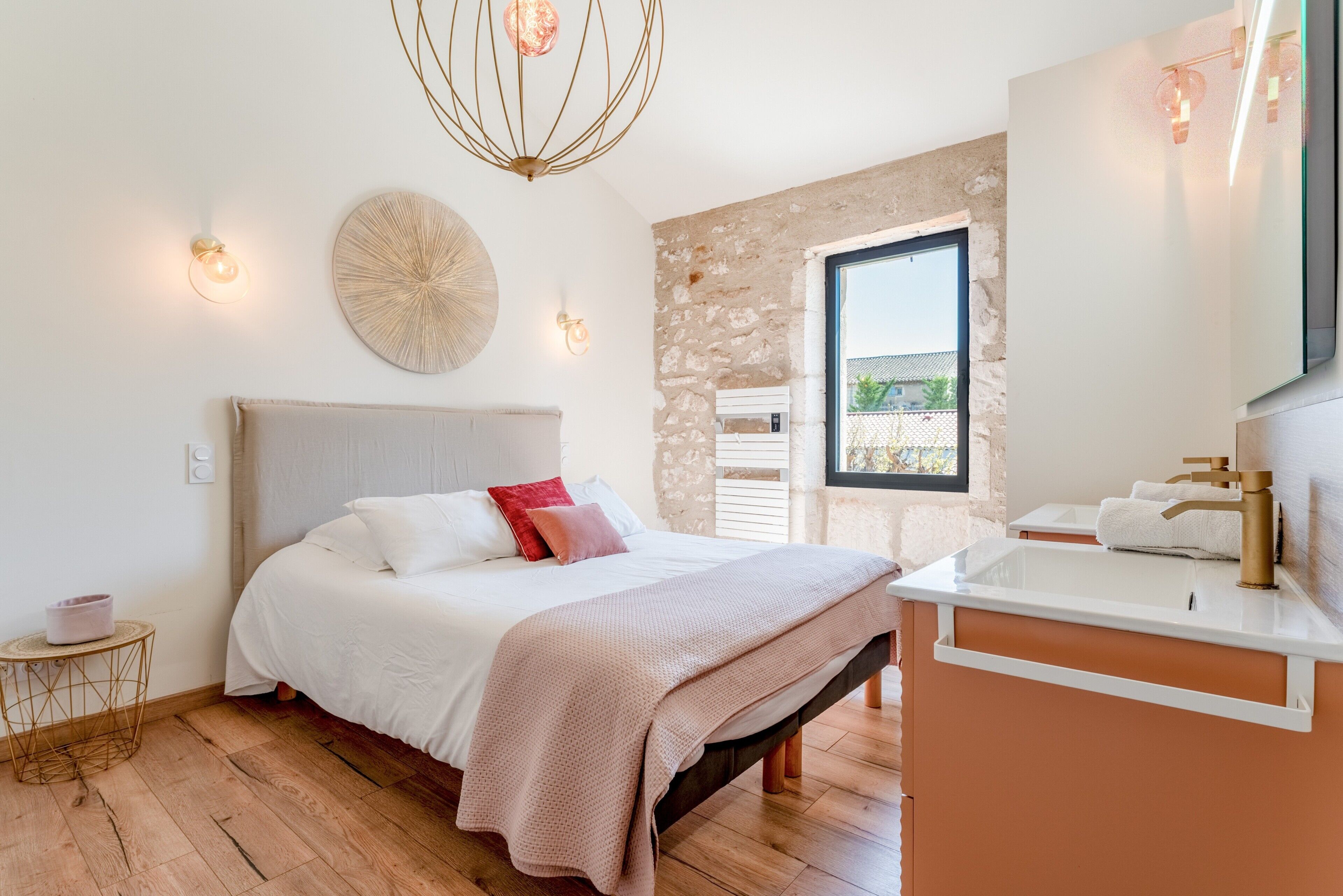 A bedroom with a bed, bedside table, and a bathroom with a sink and mirror.