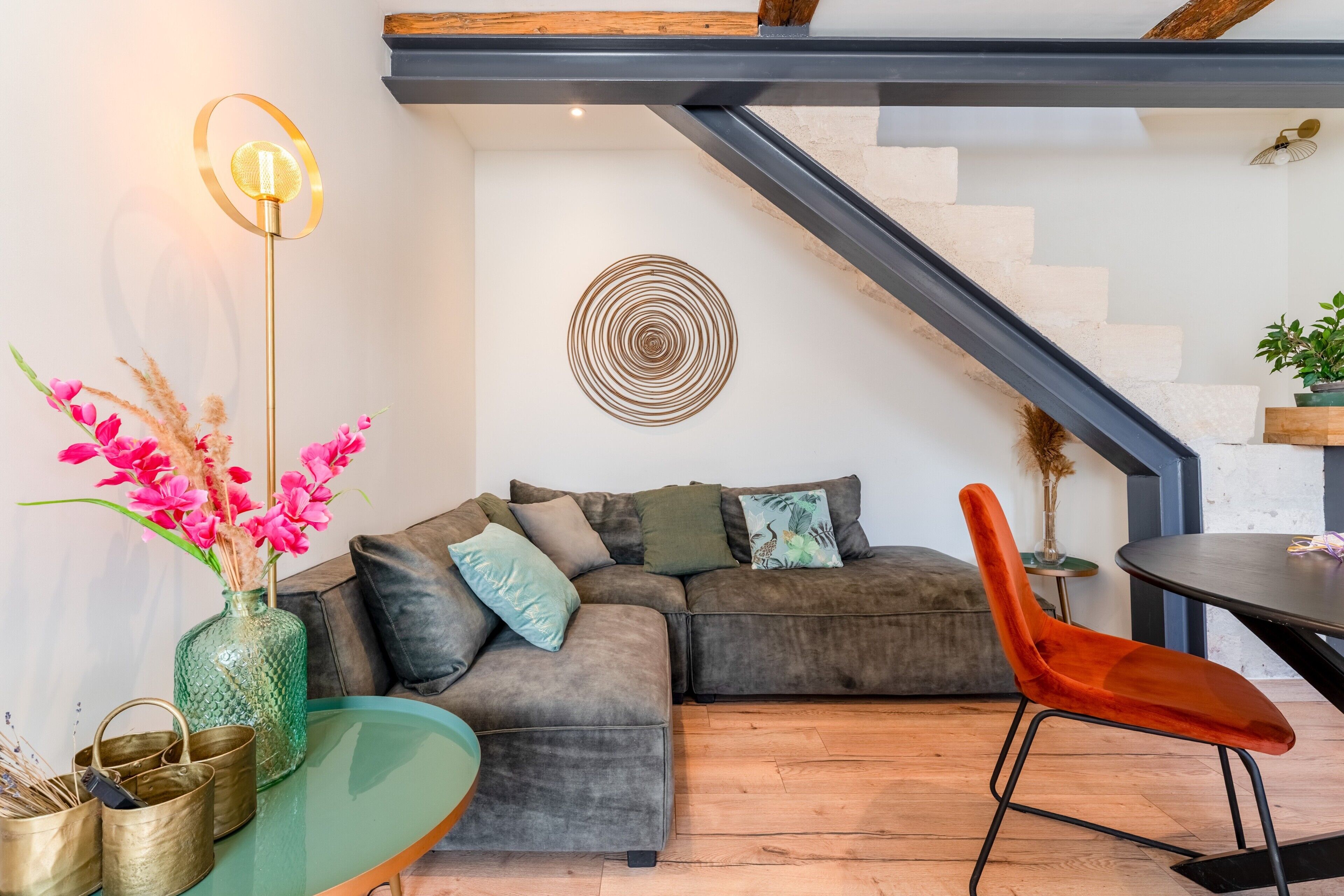 A modern living room with a sectional sofa, a glass coffee table, a red chair, a floor lamp, and a spiral wall art piece.
