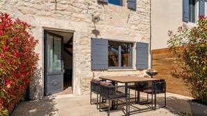 Un edificio de piedra con puerta de madera, una mesa con sillas y plantas en macetas.