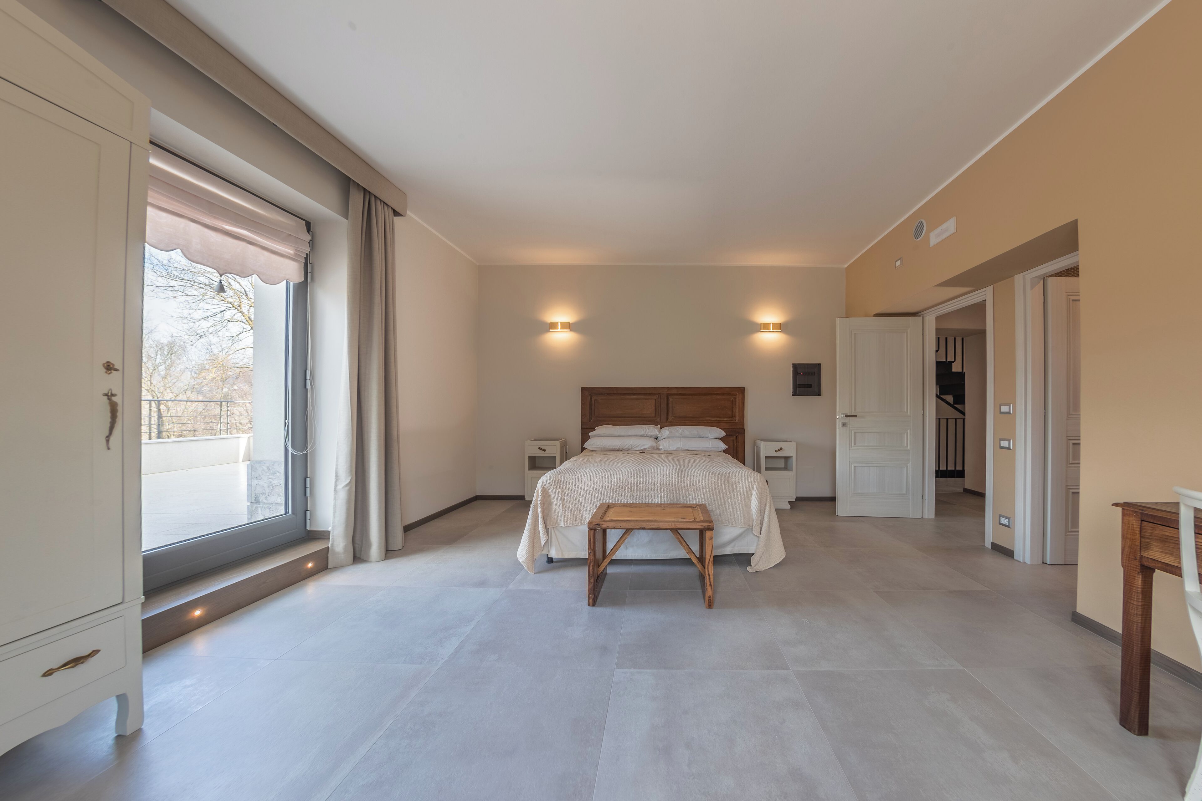 Une chambre à coucher avec un grand lit, des tables de chevet, un banc en bois et une vue par la fenêtre.