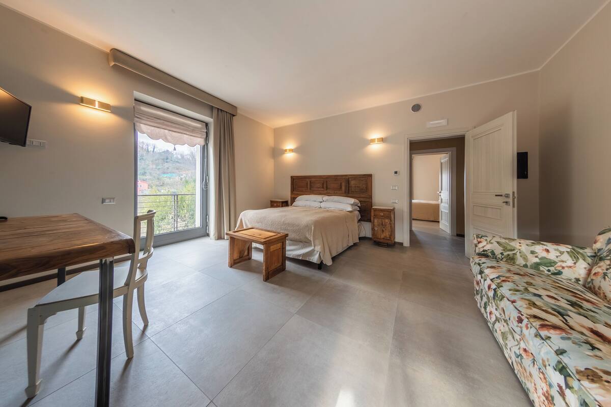 A bedroom with a bed, bedside tables, a wooden desk, a chair, and a sofa.