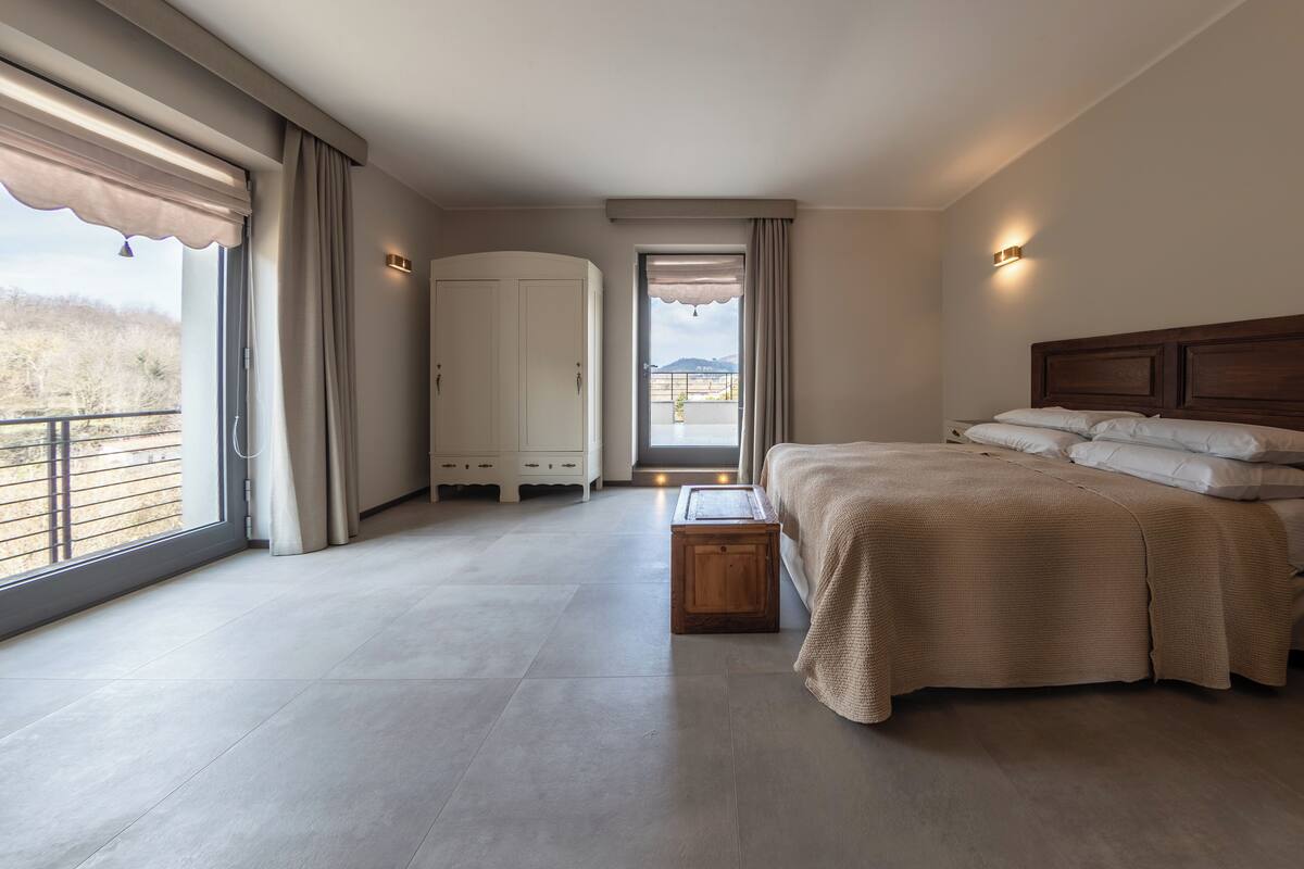 A bedroom with a large bed, a wardrobe, a small table, and a view of the outdoors through a window.