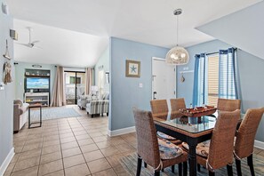 A dining area with a glass table and wicker chairs, a television in the background, and a ceiling fan. - ☀️Stunning Water Views | Easy Beach Access | Sandpiper Cove 19☀️ (Destin)