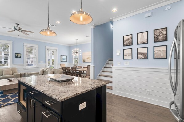A modern kitchen with a marble island, pendant lighting, and a dining area with a staircase. - 🚲 Sail & Trails | Golf Cart + 4 Bikes | Pet Friendly | 30A (Santa Rosa Beach)