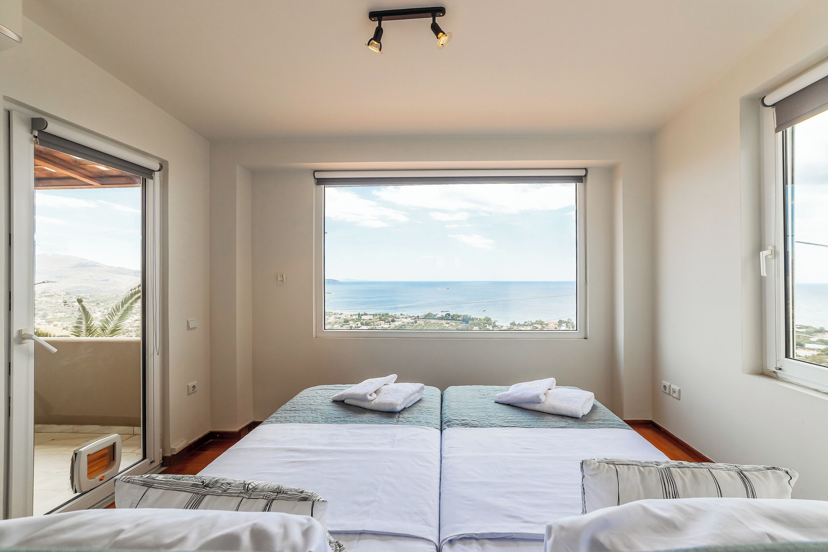 Une chambre avec deux lits, une vue sur la mer et une porte coulissante donnant sur l’extérieur.