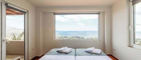 Une chambre avec deux lits, une vue sur la mer et une porte coulissante donnant sur l’extérieur.