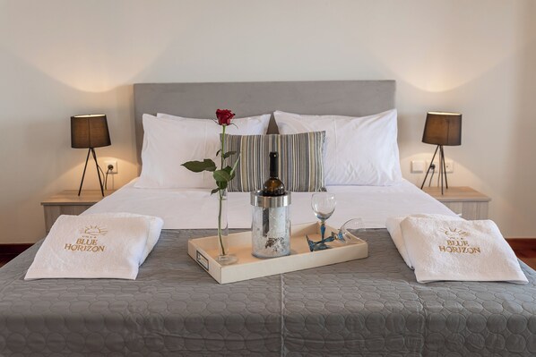 A neatly made bed with a grey quilt, a rose, a candle, and a tray with a towel and a glass. - Blue Horizon Villa (Kalyvia Thorikou)