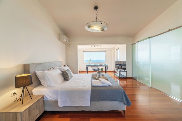 Un dormitorio moderno con cama, mesita de noche y vista al mar a través de un amplio ventanal.