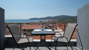 En balkon med et bord og to stole, med udsigt over en kystby og havet.