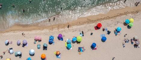 Een luchtbeeld van een strand met vele kleurrijke parasols en mensen die van het water genieten.