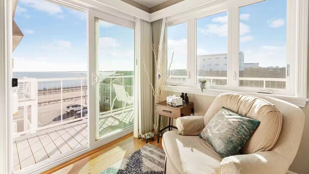 Ein geräumiger Balkon mit Glastür, eine gepolsterte Sitzecke mit Blick auf die Stadt und ein kleiner Tisch mit einer Vase.