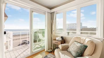 A spacious balcony with a glass door, a cushioned seating area with a view of the city, and a small table with a vase.