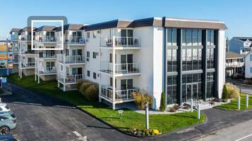 A modern multi-story residential building with balconies, large windows, and a well-maintained lawn.