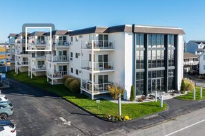 Un immeuble résidentiel moderne à plusieurs étages, doté de balcons, de grandes fenêtres et d’une pelouse bien entretenue.