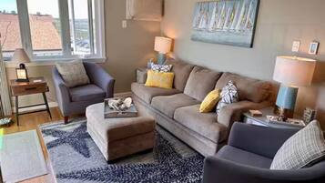 A living room with a sofa, ottoman, and armchairs, a coffee table, and two lamps.