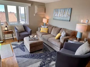 Un salon comprenant un canapé, un pouf et des fauteuils, une table basse et deux lampes.