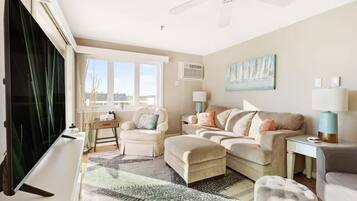 A living room with a sofa set, a TV, a ceiling fan, and a large window with curtains.