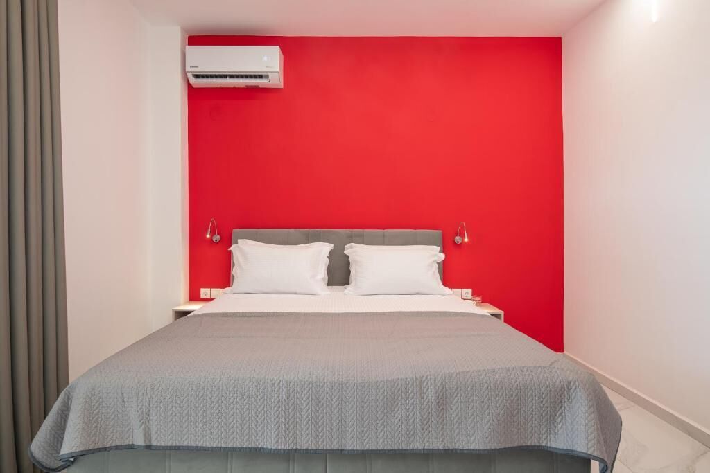 Habitación de hotel con una pared de acento roja, una cama con ropa blanca y un equipo de aire acondicionado sobre la cama.