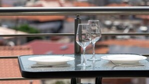 Une table avec deux verres à vin et une assiette, donnant sur une ville côtière avec des montagnes en arrière-plan.