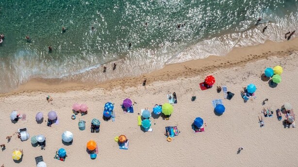 Une vue aérienne d’une plage où l’on peut voir de nombreux parasols colorés et des gens qui se baignent.