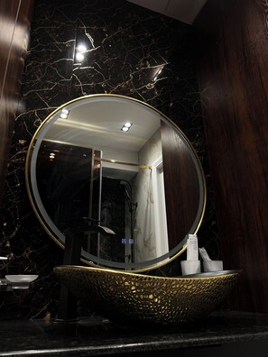 Een badkamer met een ronde spiegel, een wastafel met gouden lijst en een marmeren wand.